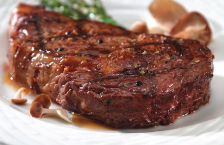 Právě ugrilovaný šťavnatý rib-eye steak na bílém talíři. 